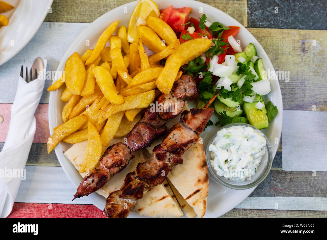 Piastra del tipico pasto cipriota. Spiedini di carne di maiale, pane pitta, patatine e insalata con tzatsiki dip. Foto Stock
