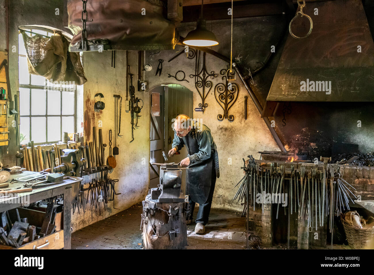 Un fabbro maschio che forma un pezzo di ferro incandescente, usando un  martello e una spazzola d'acciaio, in una giornata di sole Foto stock -  Alamy