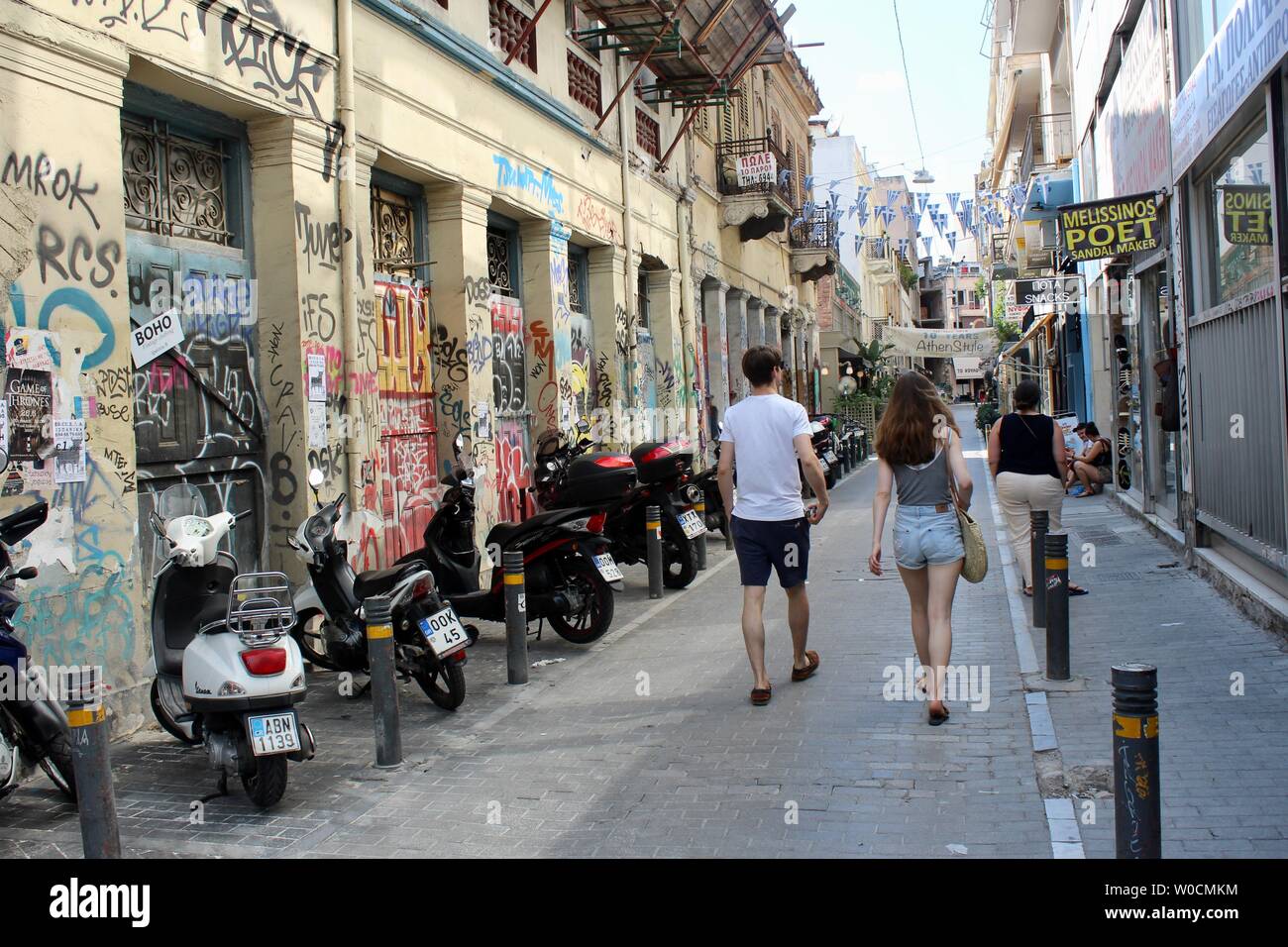 Un giovane a piedi giù per una strada coperta di graffiti e parcheggiata scooters ad Atene in Grecia Foto Stock