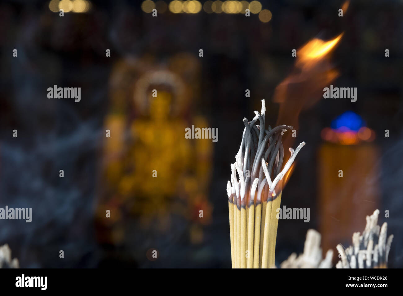 La masterizzazione di bastoncini di incenso con fuori fuoco statua del Buddha in background. Foto Stock