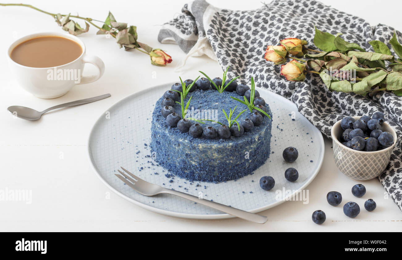 Tavolo con Blue mirtillo torta di velluto. Tazza di caffè con latte, piccola ciotola con mirtilli, sciarpa e fiori secchi, rose. Foto Stock