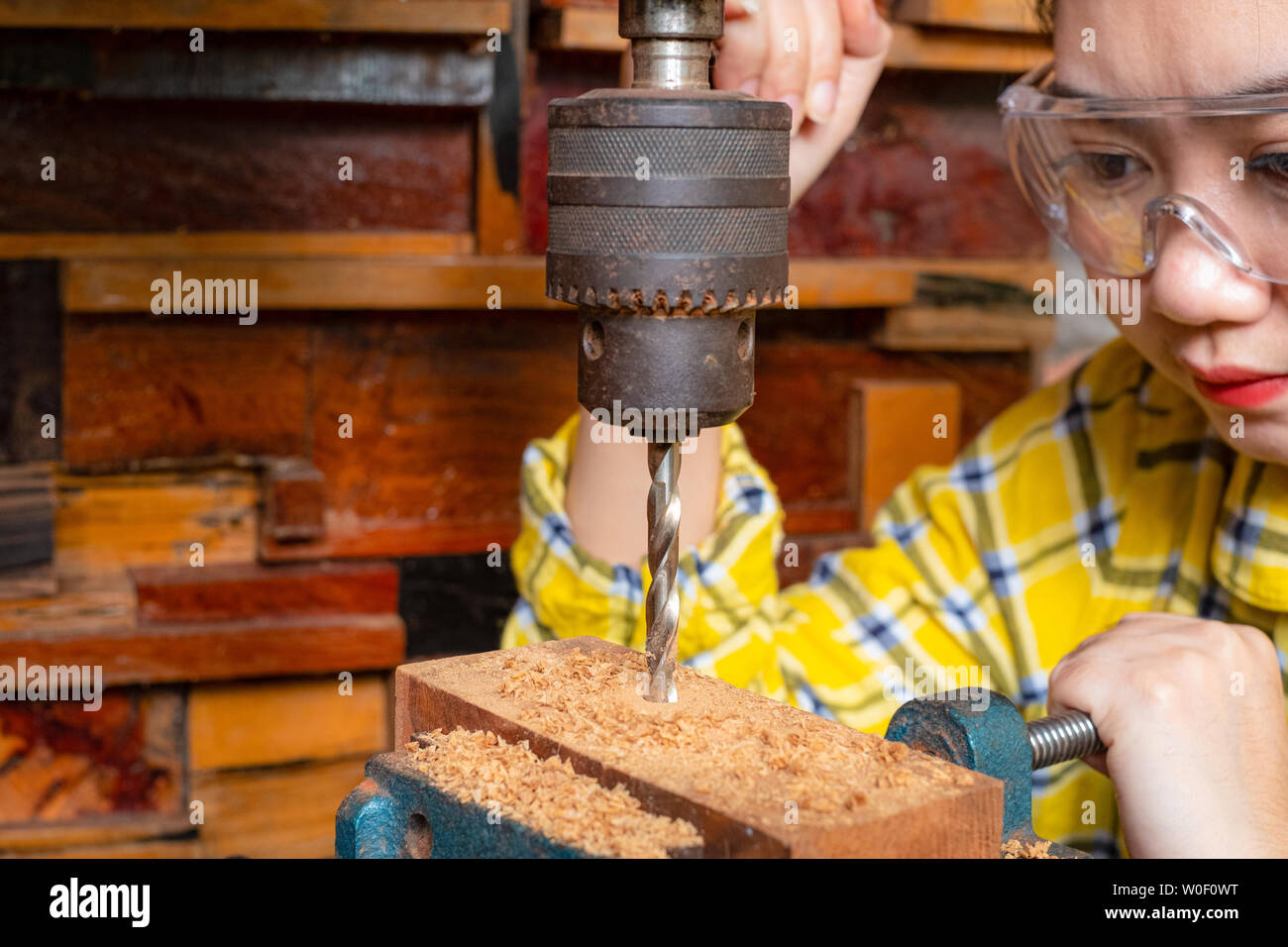 Le donne è permanente di lavoro di artigianato in legno trapano in corrispondenza di un banco di lavoro con drill premere power tools a carpenter la macchina in officina Foto Stock