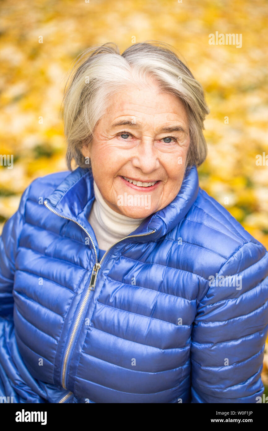 Ritratto di un smilling piuttosto senior anteriore donna foglie gialle. Foto Stock