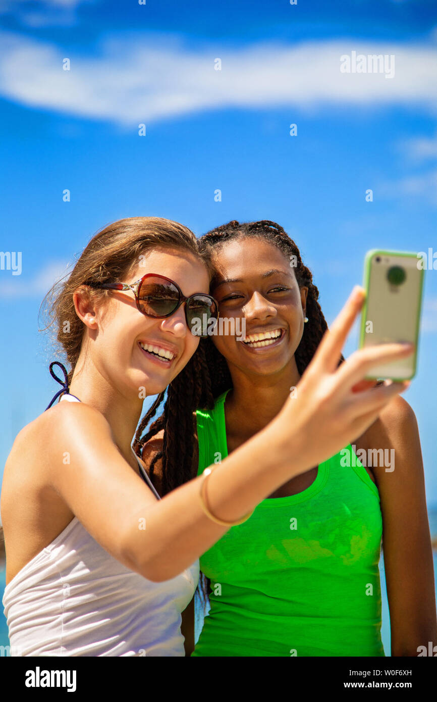 2 ragazze sorridenti tenendo un selfie contro il cielo blu sullo sfondo. Foto Stock
