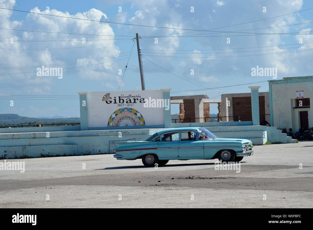 Cuba, Gibara, un vecchio blu 50s vettura americana passa di fronte al segno che celebra il bicentenario della città di Gibara Foto Stock