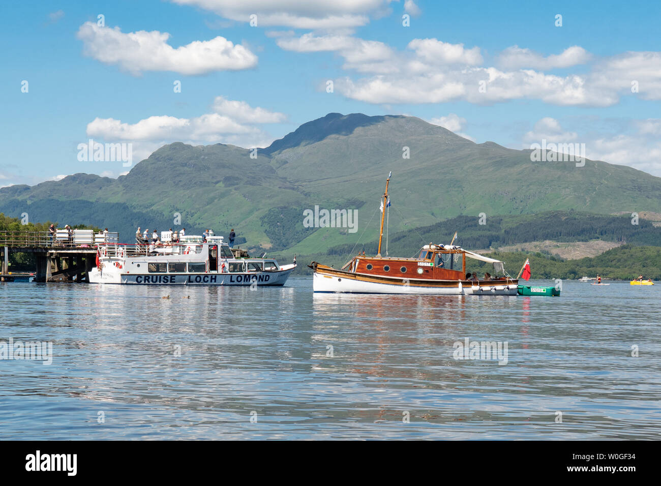 Luss, Loch Lomond Scozia, Regno Unito - 27 Giugno 2019: Regno Unito meteo - una cartolina impostazione come la gente a prendere alle acque di raffreddamento del Loch Lomond su di una teglia calda giornata Luss, al di sotto del picco di distintivo di Ben Lomond Credito: Kay Roxby/Alamy Live News Foto Stock