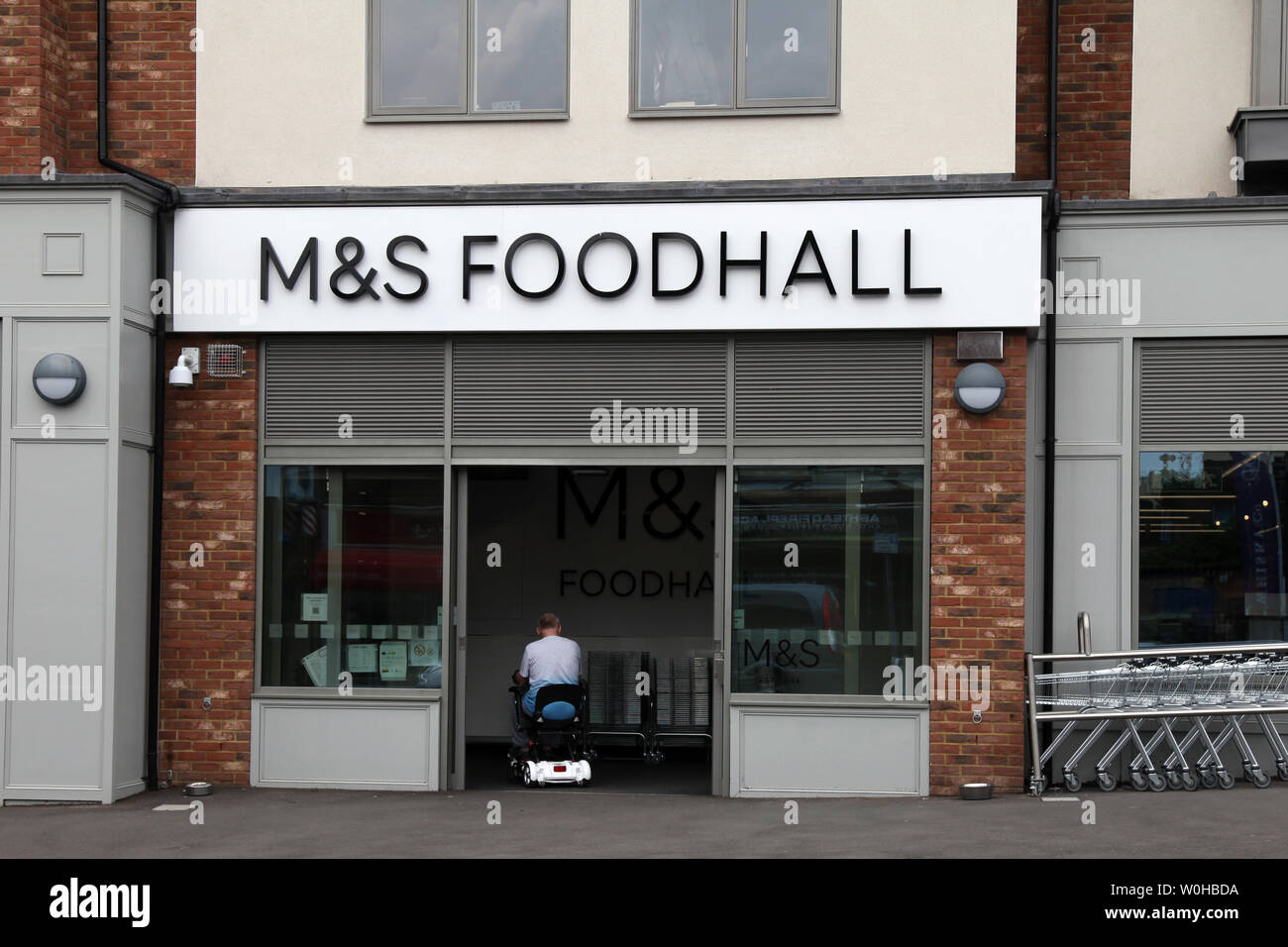 Ashtead, Surrey, Regno Unito - Marks & Spencer M&S Foodhall negozio di fronte esterno sulla strada alta con il cliente disabile di entrare su una mobilità scooter Foto Stock