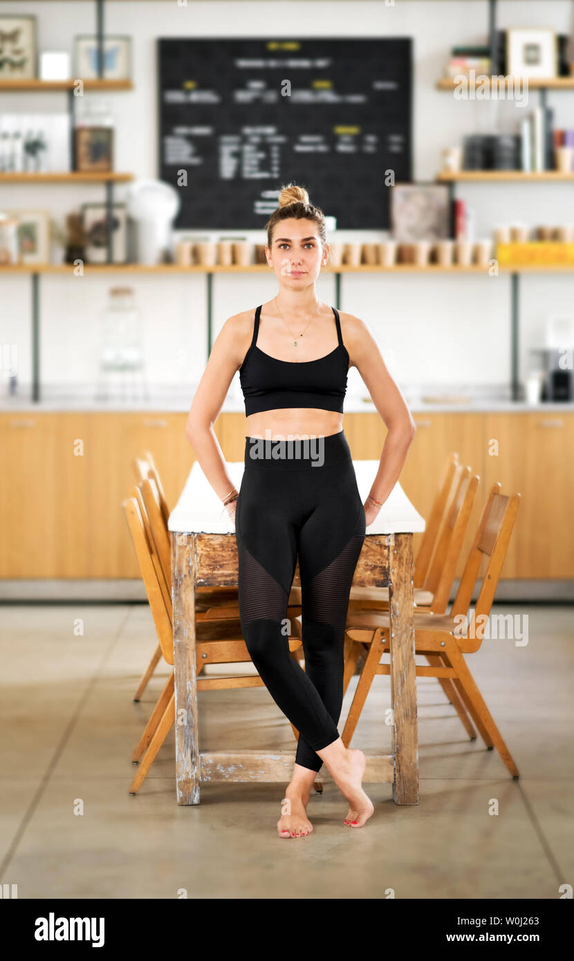 Singoli donna vestita di nero e appoggiata contro il tavolo di legno con diverse sedie sotto di esso in palestra Foto Stock