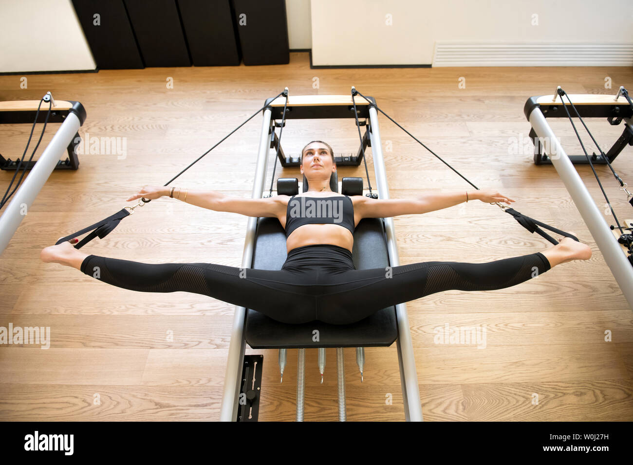 Vista aerea sulla donna adulto in abito nero utilizzando il pilates reformer macchina per allungare le gambe Foto Stock