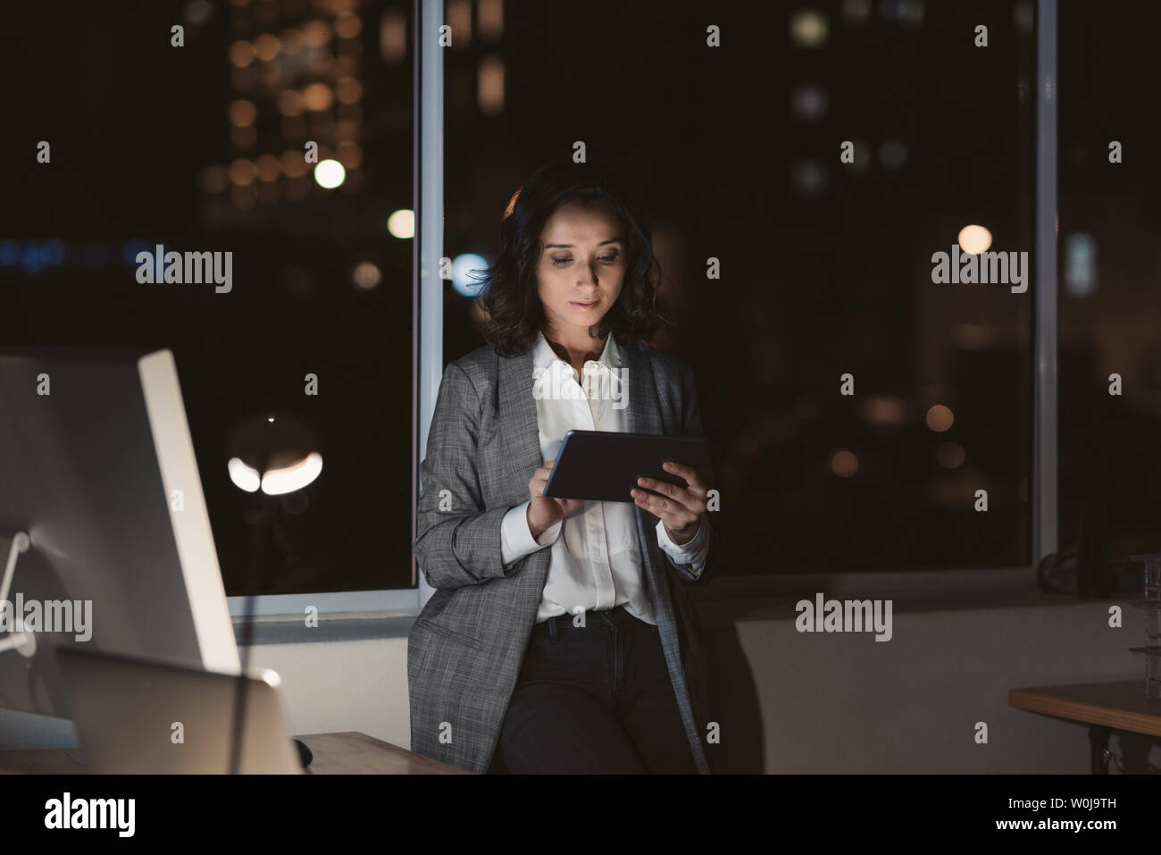 Focalizzato giovane imprenditrice in piedi da solo in un ufficio nella tarda serata di lavoro on-line con una tavoletta digitale Foto Stock