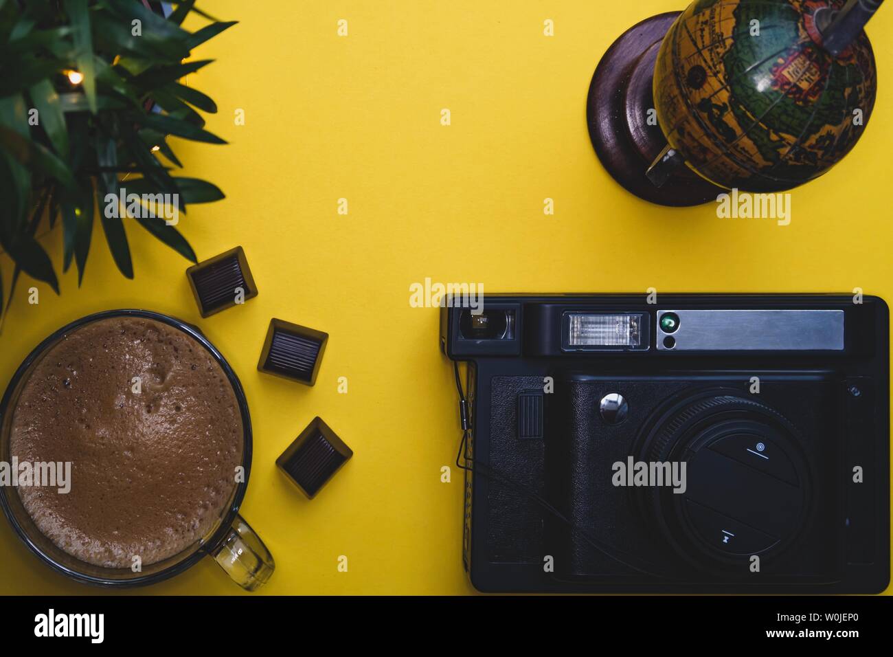 Tazza da caffè globe foto sfondo giallo verde tastiera portatile fotocamera istantanea carte spazio libero piante cioccolato Foto Stock