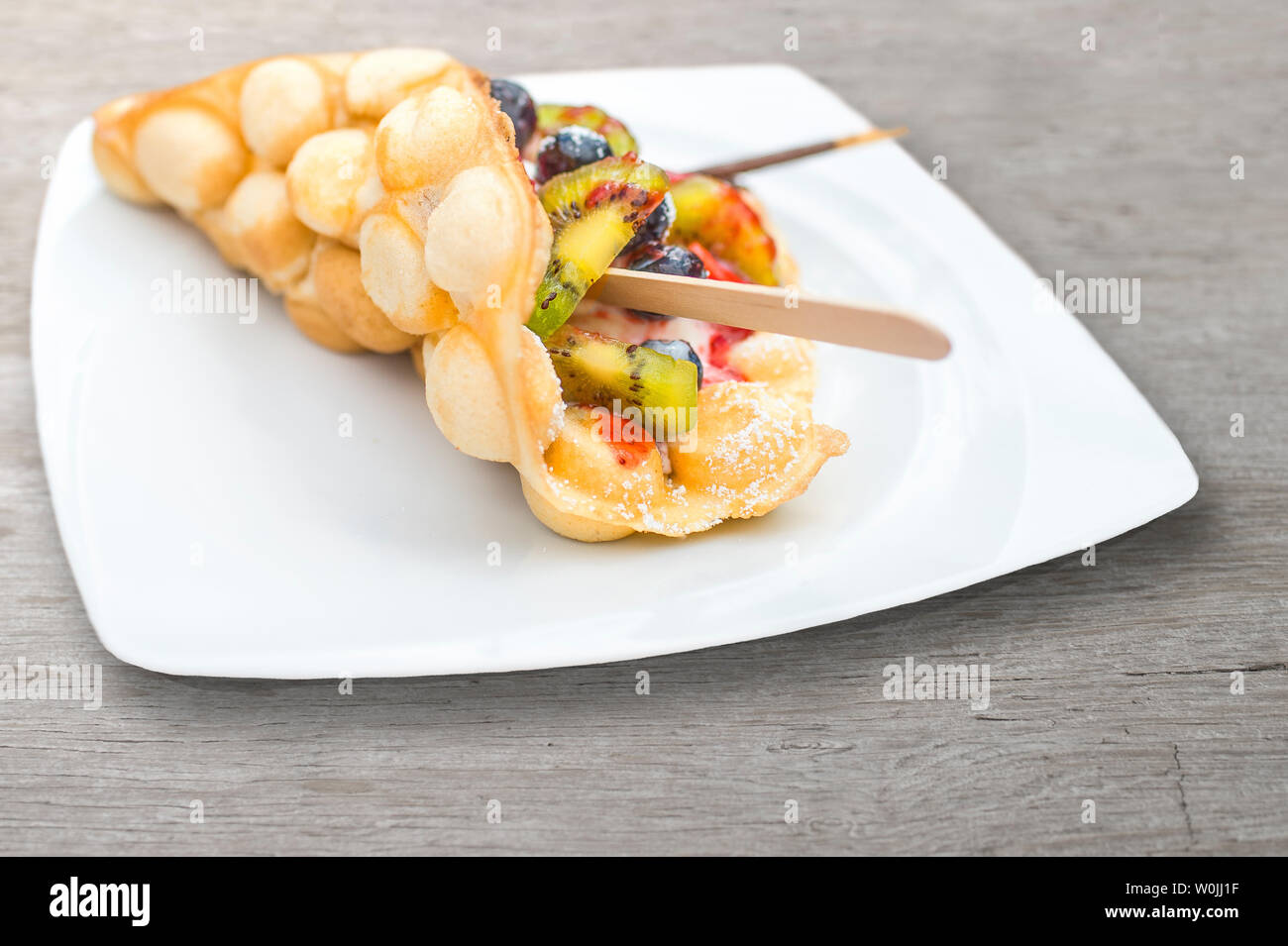 Trend bolla pasticceria cialde (uovo cialde, Hong Kong torte) con gelato e frutta fresca. Fragole, kiwi, mirtilli, salsa di fragole su bianco Foto Stock