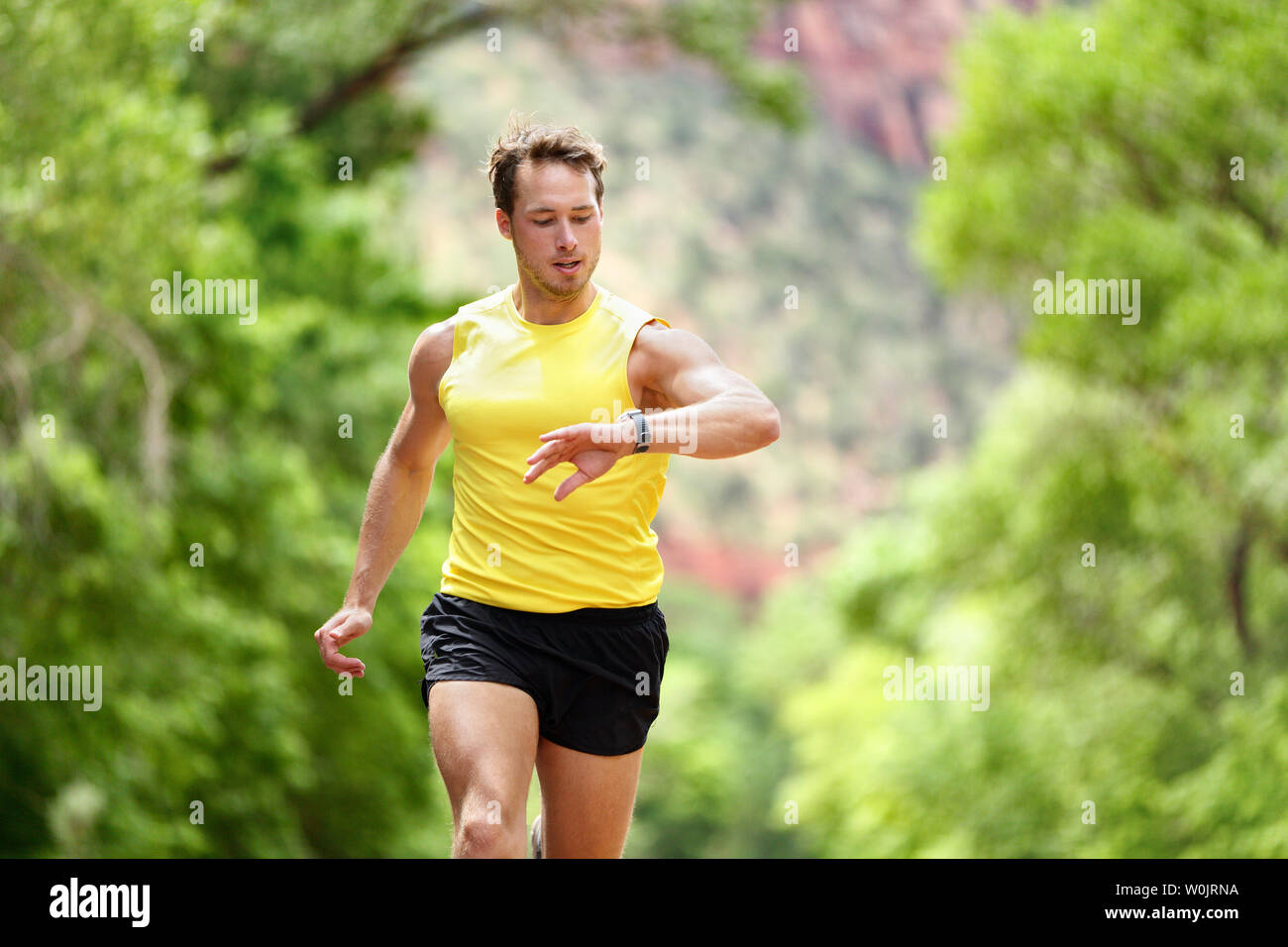 In esecuzione guardando il monitor per la frequenza cardiaca smartwatch durante l'esecuzione. Runner maschio jogging all'esterno guardando sport smart watch durante la formazione di allenamento per la maratona Correre. Montare maschio modello fitness nel suo 20s. Foto Stock