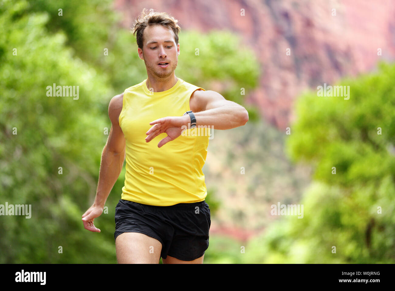 Runner guardando il monitor per la frequenza cardiaca smartwatch durante l'esecuzione. L'uomo jogging all'esterno guardando il suo sport smart watch durante la formazione di allenamento per la maratona Correre. Montare maschio modello fitness nel suo 20s. Foto Stock