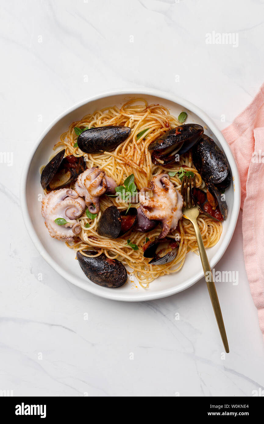 Pasta con frutti di mare e salsa di pomodoro. Spaghetti con il polpo e cozze in bianco ciotola con una forchetta e tovagliolo rosa su sfondo bianco. Concetto di seafoo Foto Stock