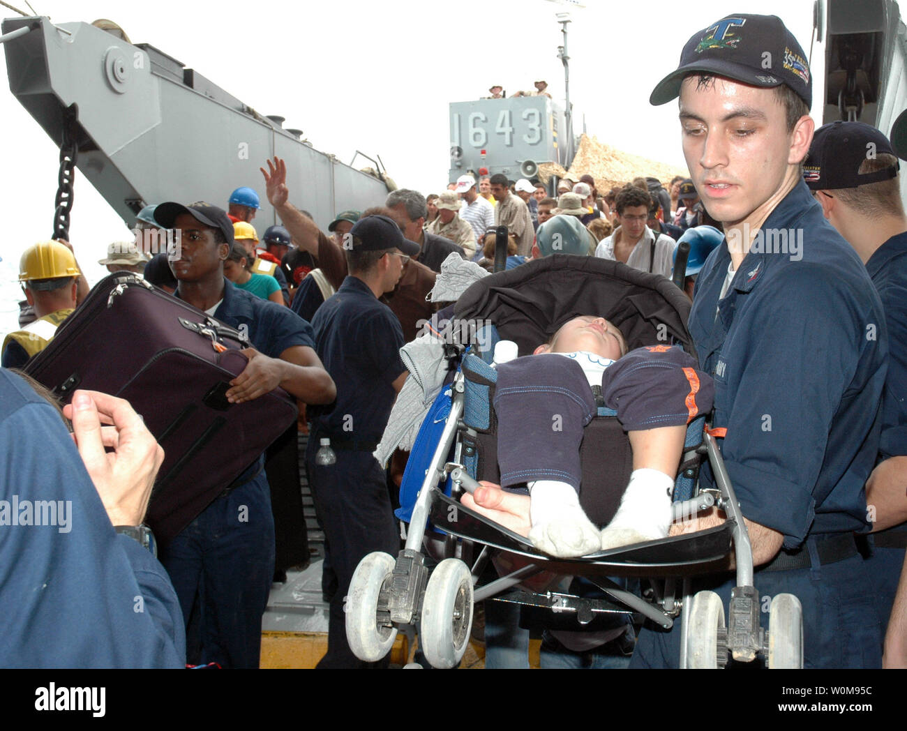 Un U.S. Navy sailor porta un bambino addormentato in un passeggino da una landing craft utility barca alla USS Trenton (LPD 14) come la nave opera al largo delle coste del Libano il 21 luglio 2006. Su richiesta degli Stati Uniti Ambasciatore in Libano e presso la direzione del Segretario della Difesa degli Stati Uniti centrali di comando e gli elementi della Task Force 59 stanno aiutando con la partenza di cittadini degli Stati Uniti dal Libano. Il Trenton è un trasporto anfibio che è usato per trasportare e terreni di Marines, le loro attrezzature e forniture avviato dal cuscino d'aria o convenzionali di landing craft, veicoli anfibi, hel Foto Stock