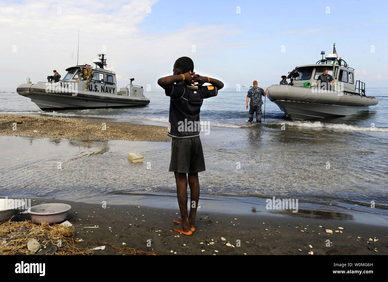 Un ragazzo haitiano orologi come rigida-hull imbarcazioni gonfiabili dal dock anfibio navi da sbarco USS Fort McHenry (LSD 43) e USS Carter Hall (LSD 50) arrivano a riva il 19 gennaio 2010 presso la speranza nuova missione a Bonel, Haiti. Il multi-purpose Amphibious Assault nave USS Bataan (LHD 5) è sulla stazione di Haiti con il dock di anfibio navi da sbarco USS Fort McHenry (LSD) 43 USS Gunston Hall (LSD 44) e USS Carter Hall (LSD 50) Supporto di funzionamento risposta unitaria, un giunto di assistenza umanitaria missione ad Haiti a seguito di una magnitudine 7.0 su gen. 12. UPI/Kristopher Wilson/STATI UNITI Navy Foto Stock