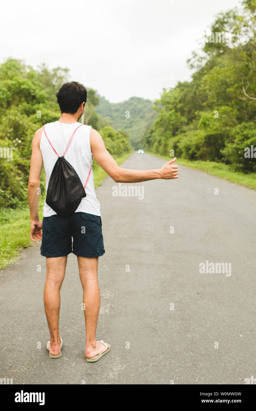 Giovane uomo autostop sulla strada di montagna in estate Foto Stock