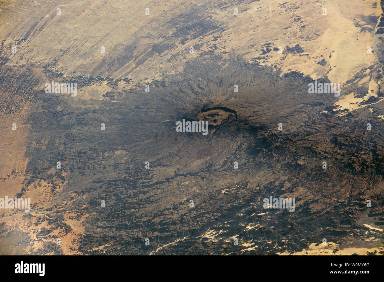 Un astronauta a bordo della Stazione Spaziale Internazionale (ISS) ha preso questa fotografia obliquo di uno dei grandi vulcani trovata nel Sahara centrale deserto su ottobre 22, 2017. Emi Koussi è il cratere scuro e il cono che occupa la maggior parte dell'immagine. Il dark lave eruttata dal vulcano in contrasto con la luce circostante e tonalità di sabbia e roccia. Per la scala, la Emi Koussi cratere è da 7.5 a 9.5 miglia. Il suo cono sale così in alto al di sopra della pianura circostante (2300 metri o 7.500 piedi) che deflette i venti dominanti, che curva intorno alla montagna mass. Emi Koussi è una di una linea di trend dei vulcani Foto Stock Un astronauta a bordo della Stazione Spaziale Internazionale (ISS) ha preso questa fotografia obliquo di uno dei grandi vulcani trovata nel Sahara centrale deserto su ottobre 22, 2017. Emi Koussi è il cratere scuro e il cono che occupa la maggior parte dell'immagine. Il dark lave eruttata dal vulcano in contrasto con la luce circostante e tonalità di sabbia e roccia. Per la scala, la Emi Koussi cratere è da 7.5 a 9.5 miglia. Il suo cono sale così in alto al di sopra della pianura circostante (2300 metri o 7.500 piedi) che deflette i venti dominanti, che curva intorno alla montagna mass. Emi Koussi è una di una linea di trend dei vulcani Foto Stock
