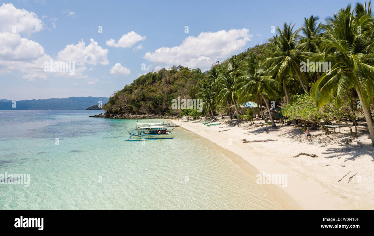 Fantastico paesaggio tropicale nelle Filippine. Tradizionale barca filippino parcheggiata in un sognato spiaggia con palme, sabbia bianca e acque azzurre Foto Stock