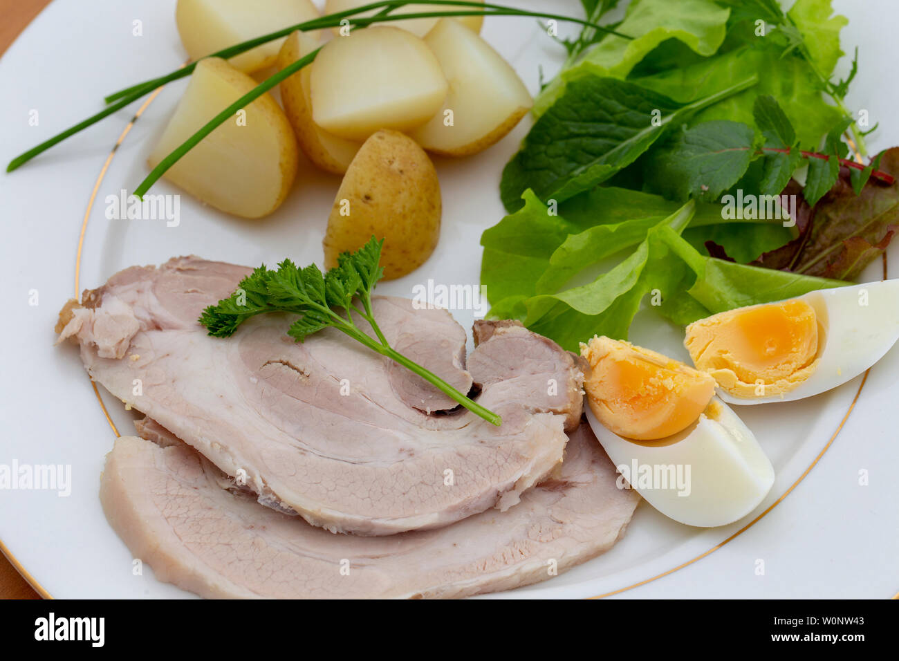 Elevato angolo di visione del freddo arrosto di maiale slice la cena con foglie di insalata, erba cipollina, uovo e patate novelle bollite Foto Stock