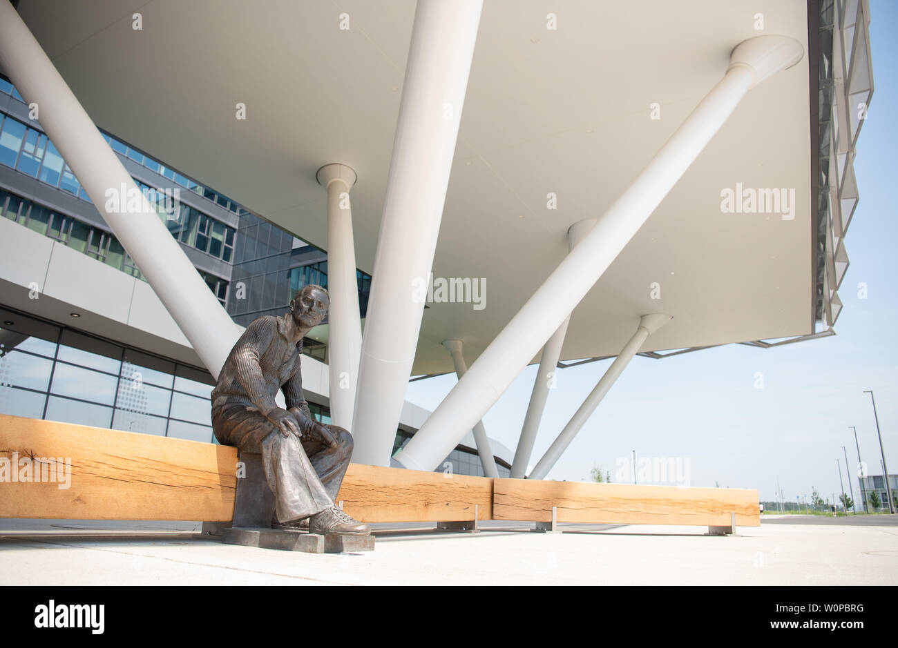 Herzogenaurach, Germania. Il 26 giugno, 2019. Una statua del Fondatore Adolf "" Adi Dassler è posizionata nella parte anteriore del nuovo edificio per uffici "Arena" della sporting goods costruttore "adidas". Nel settantesimo anno della sua esistenza, lo Sporting Goods fabbricante si trasferì nel nuovo campus e l'edificio principale, il "Arena", costruito come uno stadio presso la sua sede centrale a Herzogenaurach. Credito: Nicolas Armer/dpa/Alamy Live News Foto Stock