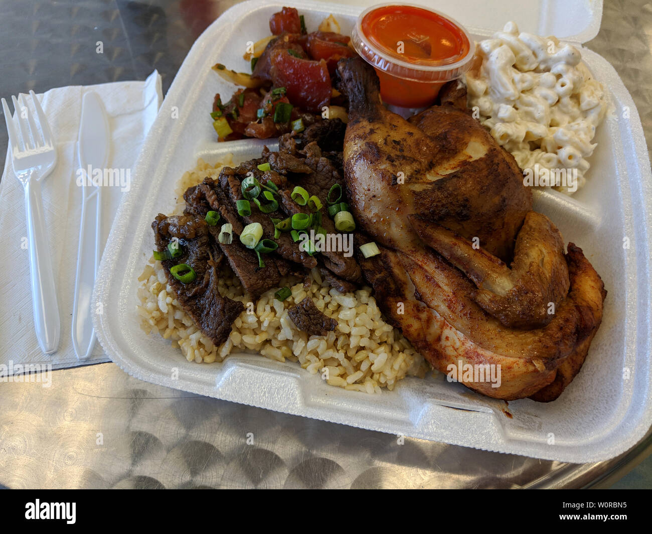 HFK piastra mista - pollo, manzo, Poke con riso e insalata di Mac plus la salsa calda sul tavolo di plastica con coltello e forchetta sul tovagliolo. Foto Stock