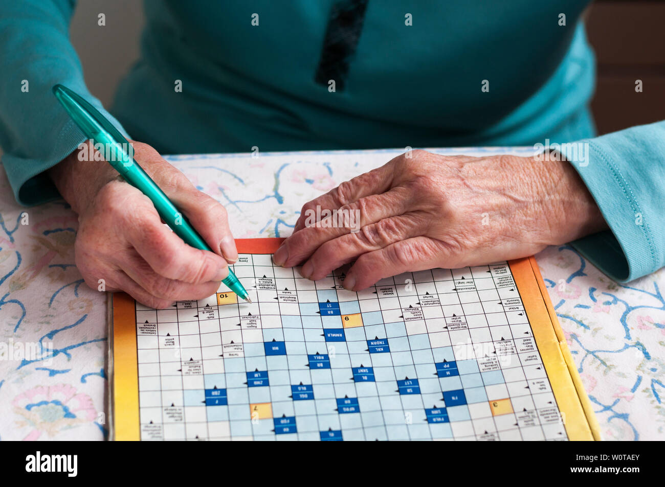 Seniorin sitzt un einem Tisch und loest Kreuzwortraesel. Foto Stock