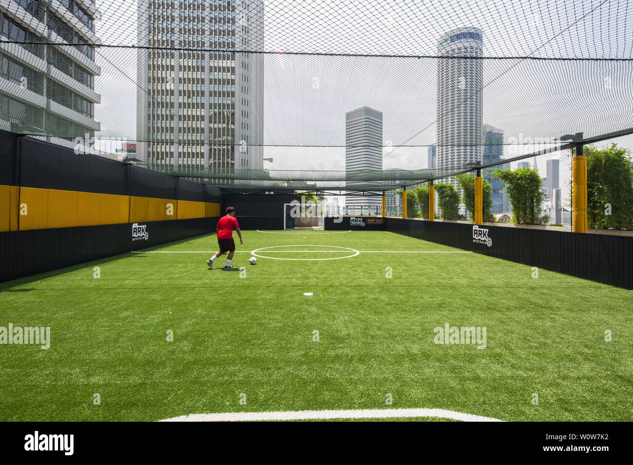 In un pomeriggio soleggiato, un uomo in camicia rossa va a un calcio al pallone in campo futsal al Funan Mall, Singapore Foto Stock
