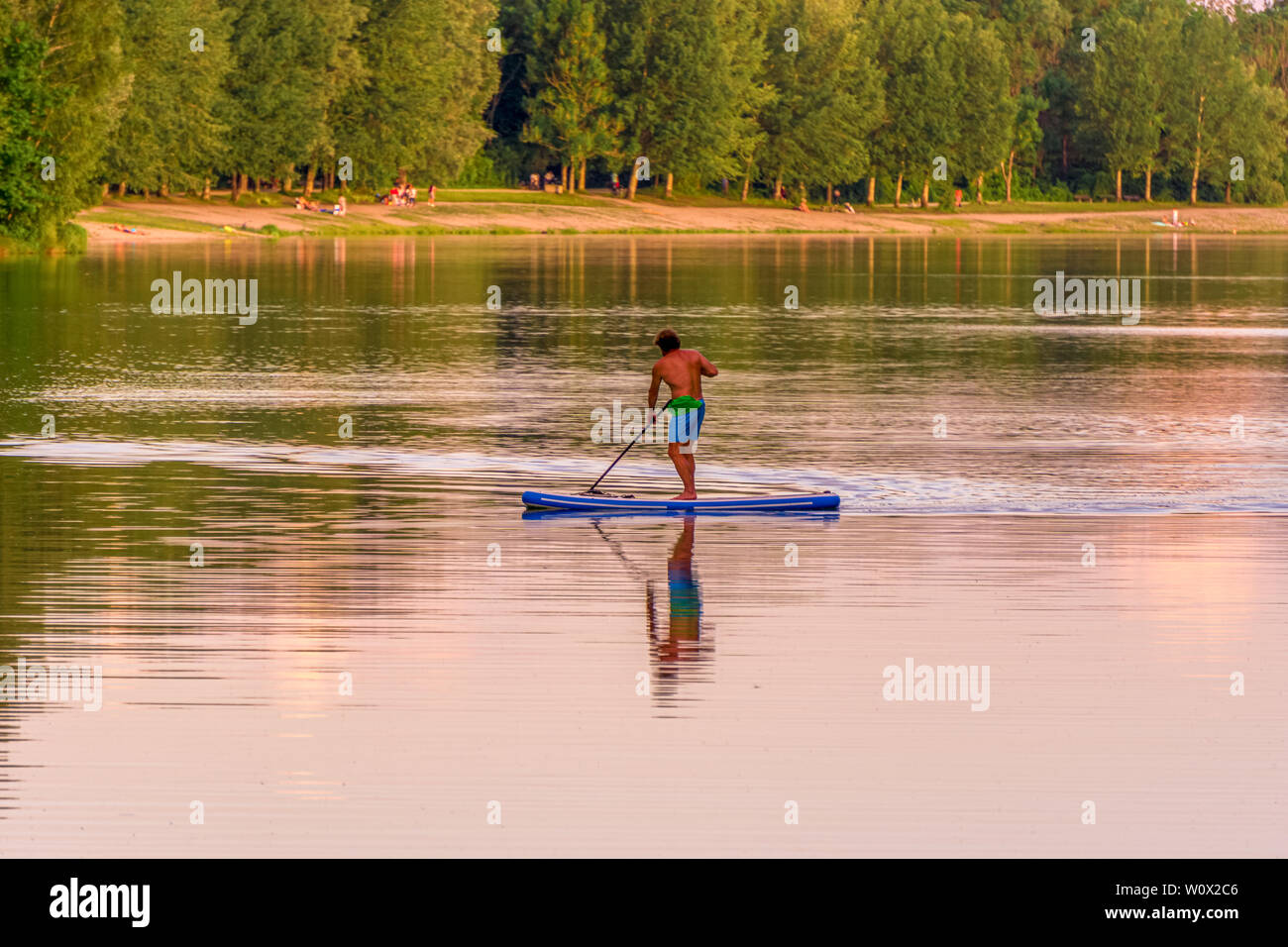 Immagine di stand up paddleboarding uomo su un lago durante il tramonto Foto Stock