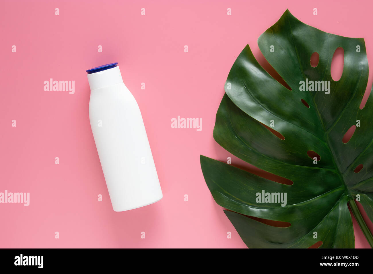 Natura cosmetica skincare concetto. bianco bottiglia cosmetico contenitore con etichetta vuota per il branding mock up, decorare con verde foglie tropicali su Pink b Foto Stock