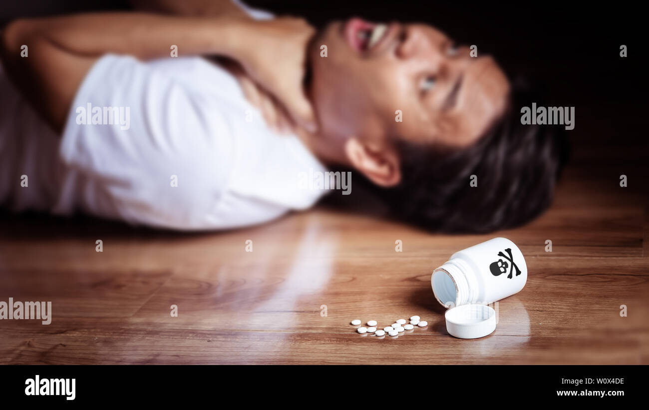 L uomo è sdraiato sul pavimento della stanza con i sintomi della tortura da mangiare veleno per suicidio, bottiglia bianca con la croce il logo cranio cade sul pavimento. p Foto Stock