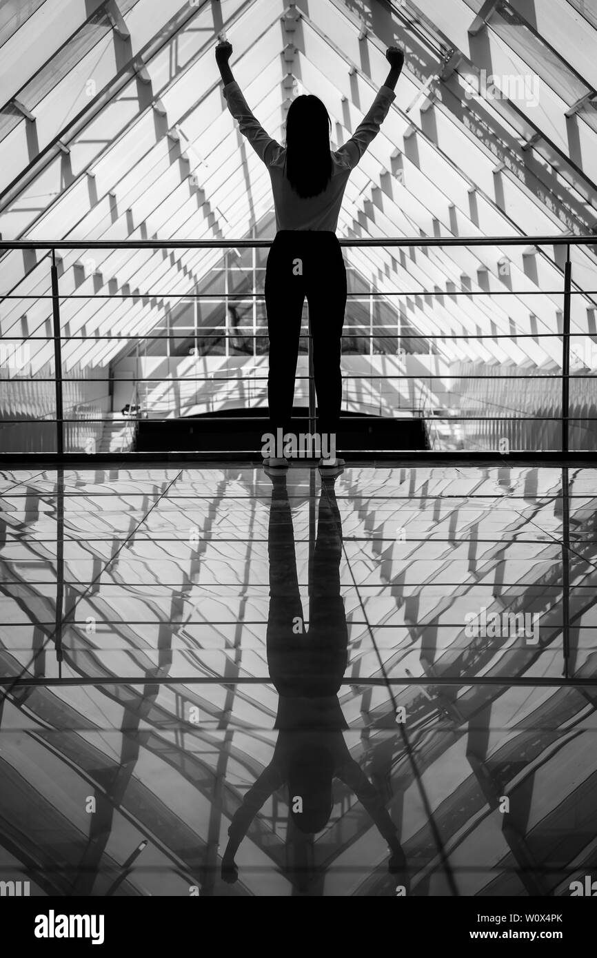 Donna di successo. Felice giovane donna mani in salita fino al cielo. Nel grande centro business Foto Stock