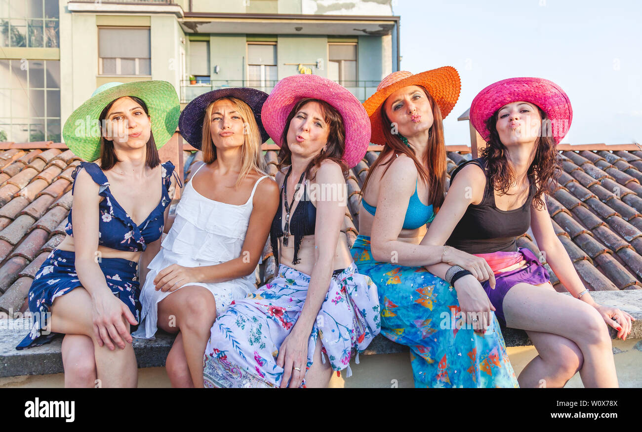 Il gruppo di amici di sesso femminile in vacanza seduti sui tetti in bikini e pareo mandano baci al tramonto - Nozione di celebrazioni e vacanze Foto Stock