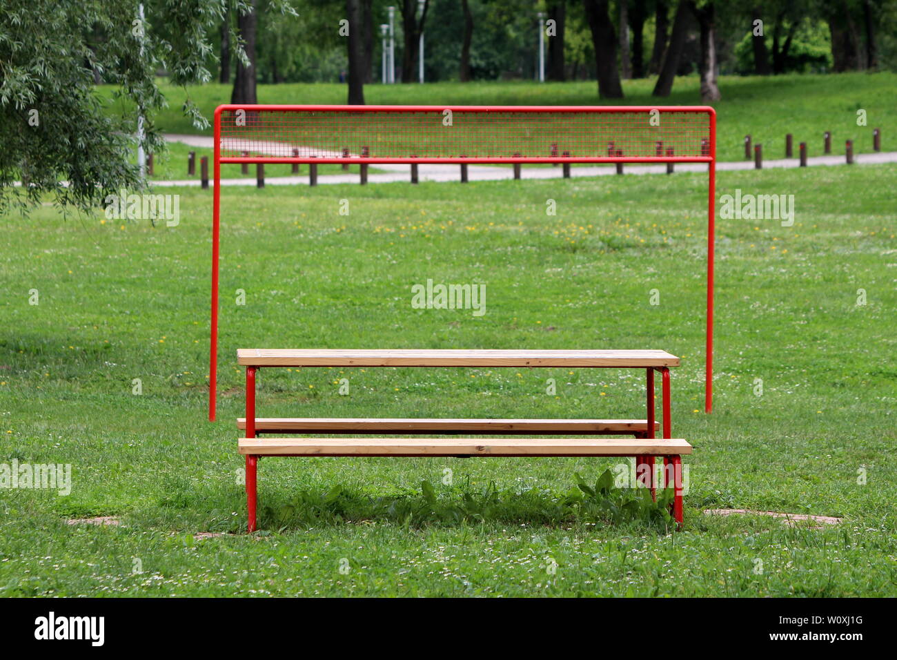 Parco pubblico di tavolo e panche nella parte anteriore del telaio di metallo pallavolo net circondato da erba non tagliata e gli alberi nel parco locale sulla calda soleggiata giornata di primavera Foto Stock