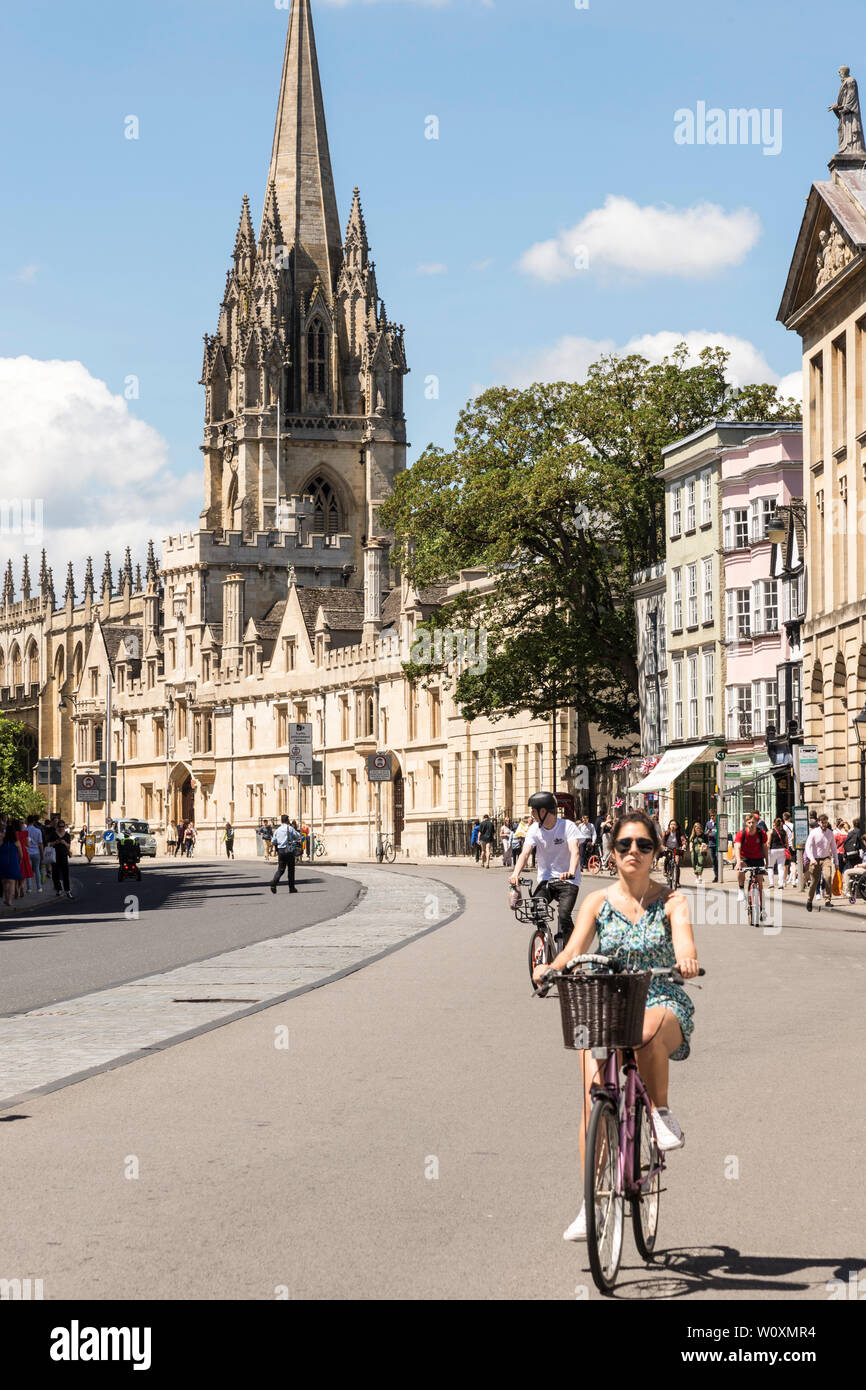 Guardando lungo High St verso la chiesa di St Mary come ciclisti cavalcare lungo su una bella e soleggiata giornata estiva nella famosa città universitaria di Oxford. Foto Stock