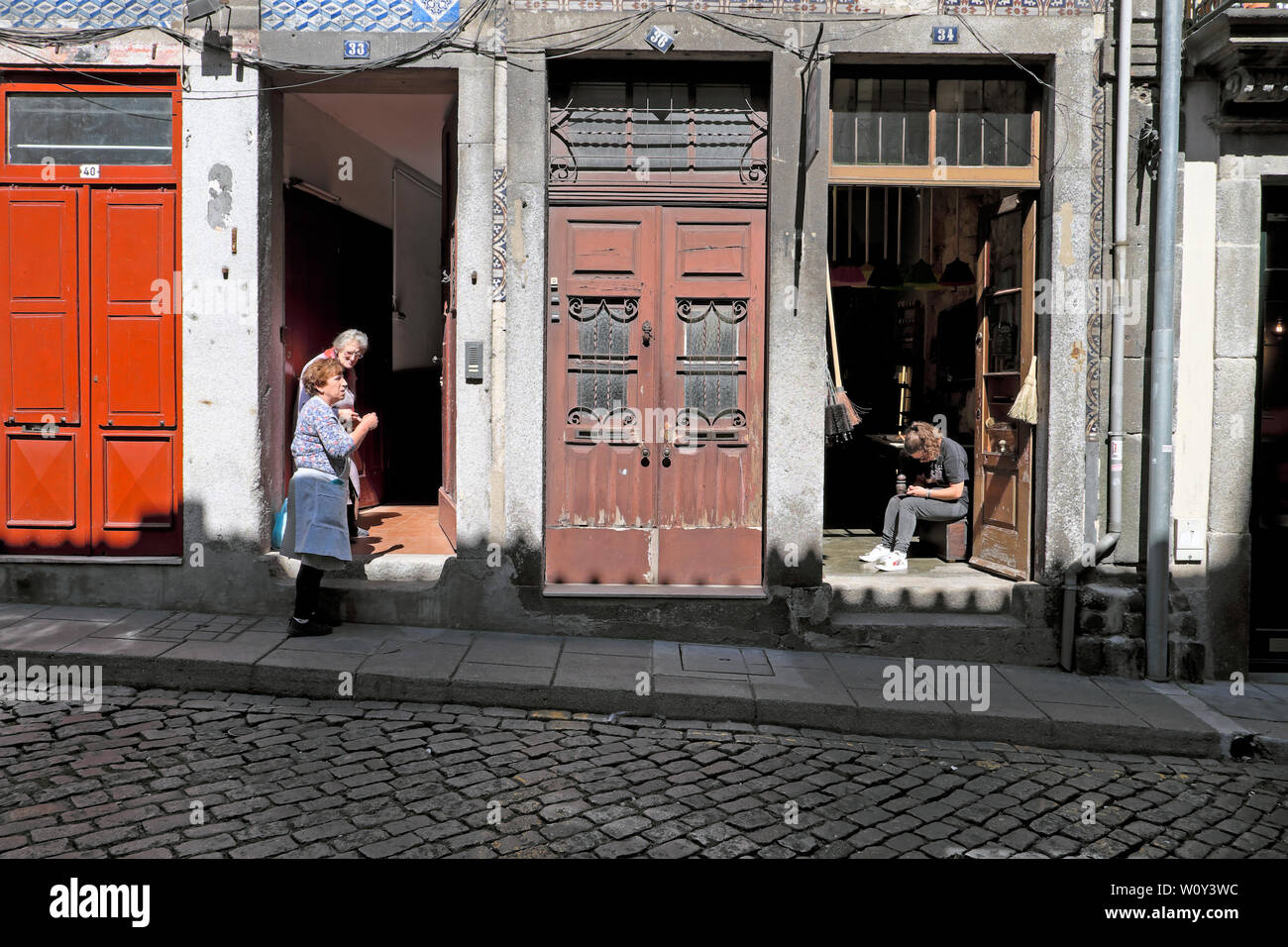 Porto vicini due donne anziane in chat a pochi passi e la giovane donna seduta da aprire la porta del negozio in una strada di Oporto portogallo Europa KATHY DEWITT Foto Stock