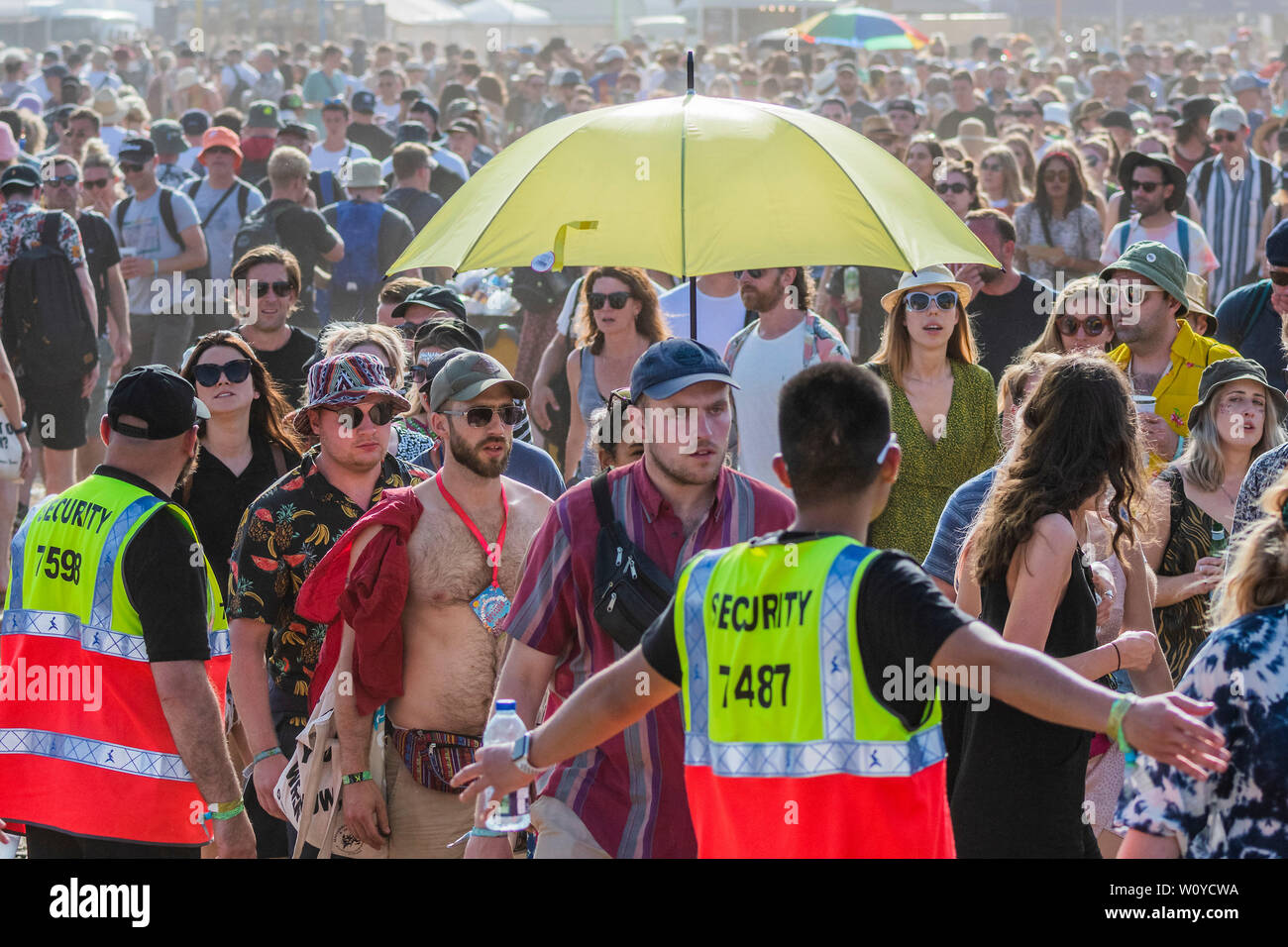 Pilton, Somerset, Regno Unito. Il 28 giugno 2019. Seciurity tenta invano di convincere la gente a haed fino alla cima di una collina al retro della piramide area - nel calore vi è una continua ricerca di acqua e molte persone portano ombrelloni, o ombrelloni come ombrelloni - Il 2019 Festival di Glastonbury, azienda agricola degna. Glastonbury. Credito: Guy Bell/Alamy Live News Foto Stock