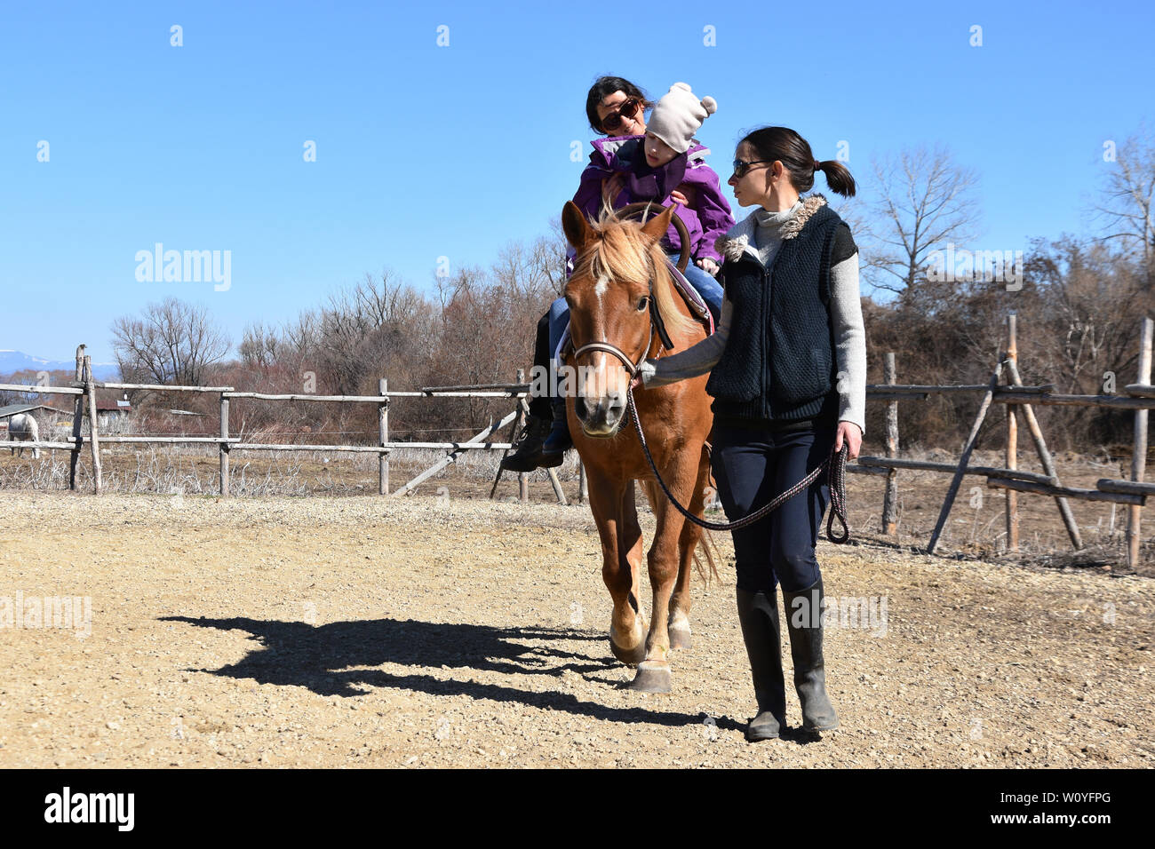 Equitazione La terapia per bambini portatori di handicap. Ragazza con paralisi cerebrale su un cavallo con il suo terapeuta, la giovane madre che conduce il cavallo Foto Stock