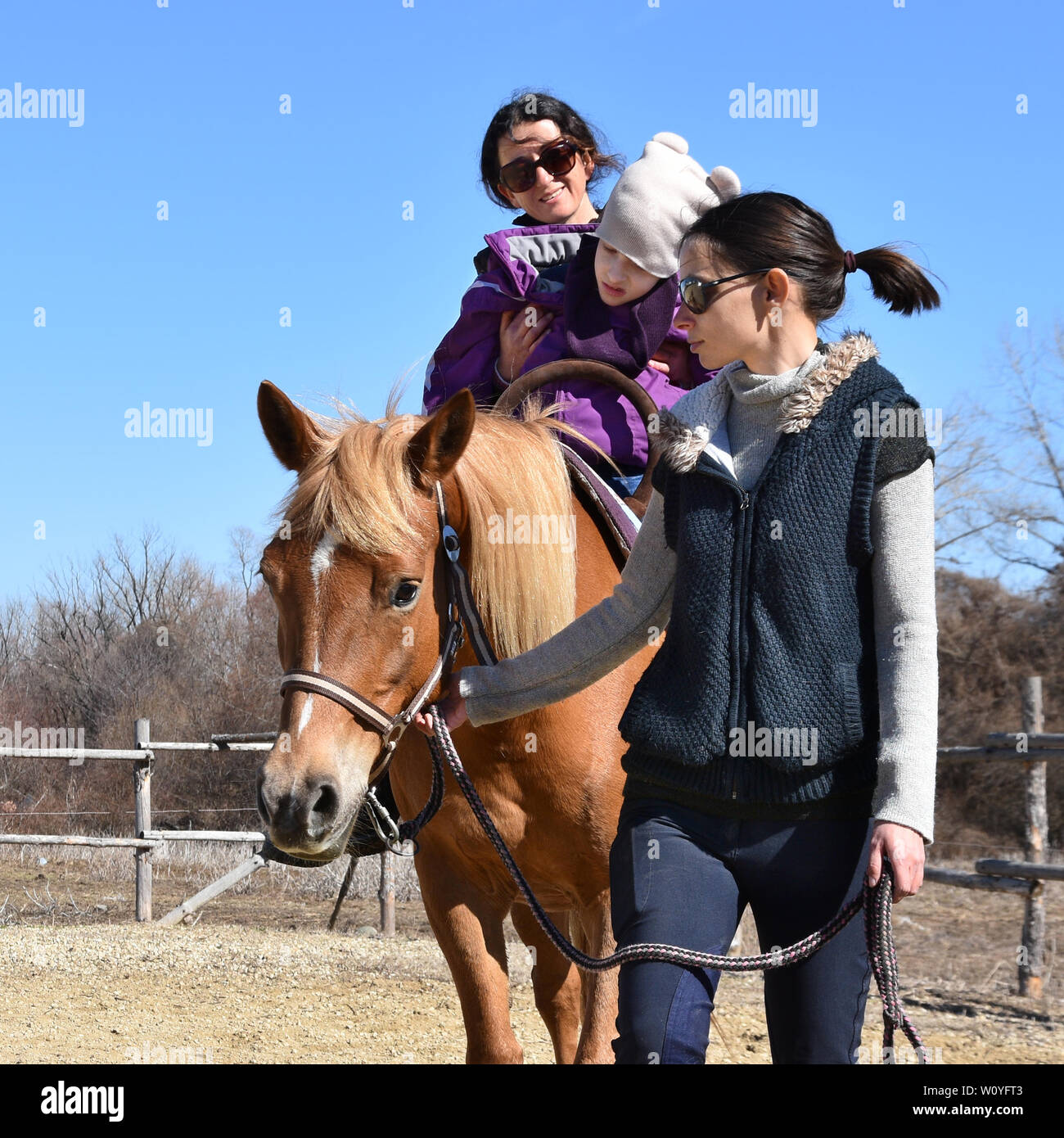 Equitazione La terapia per bambini portatori di handicap. Ragazza con paralisi cerebrale su un cavallo con il suo terapeuta, la giovane madre che conduce il cavallo Foto Stock