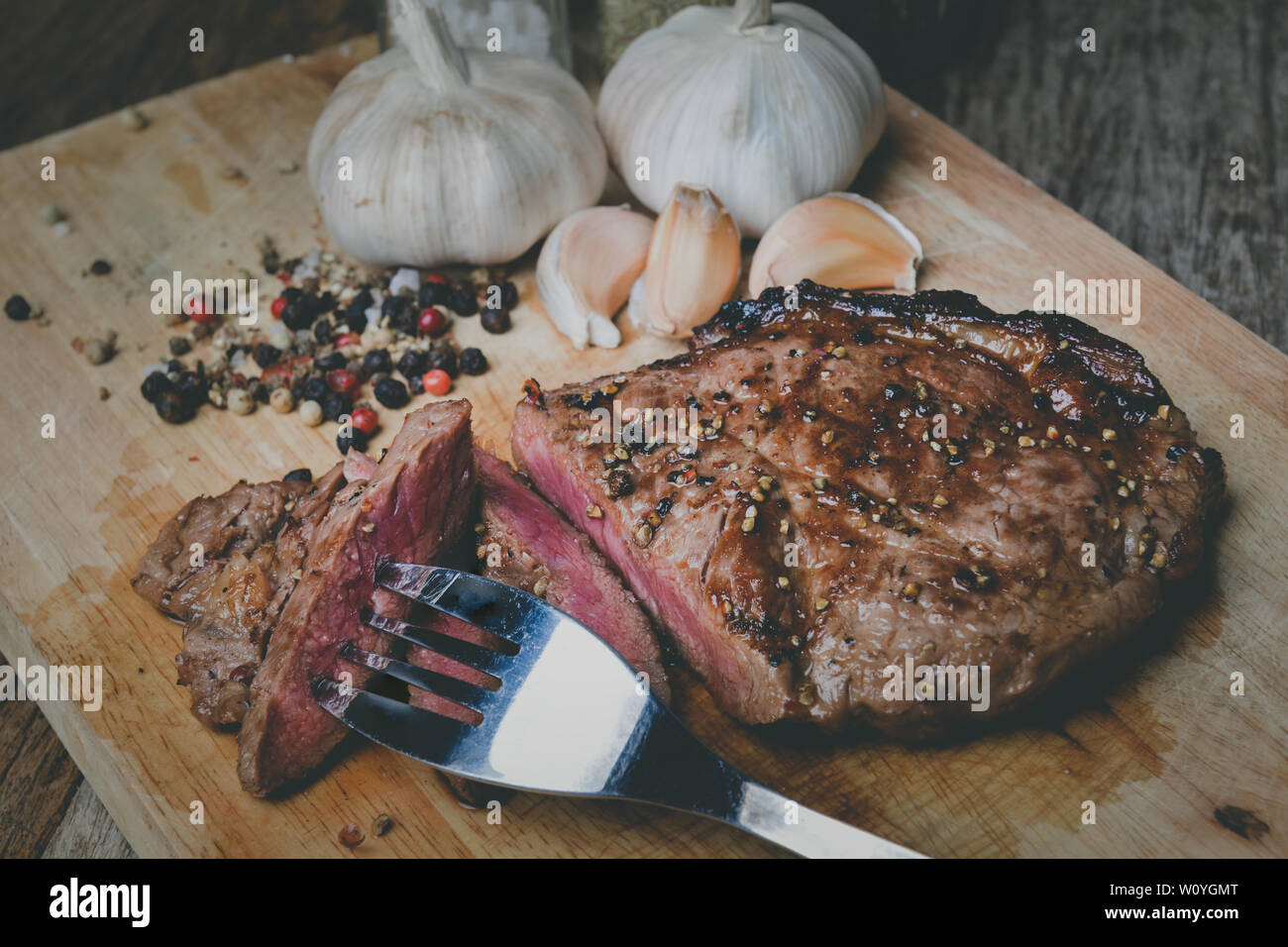 Di medie pepe bistecca fetta tagliata sul piatto di legno con spezie condimento in grigio scuro e di illuminazione del tono. Foto Stock