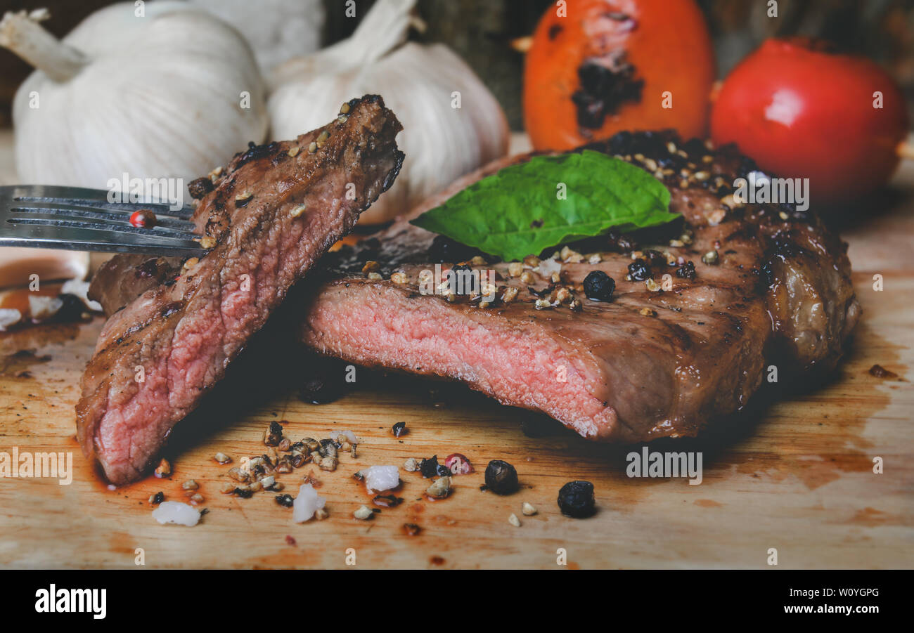 Di medie pepe bistecca fetta tagliata sul piatto di legno con spezie condimento in grigio scuro e di illuminazione del tono. Foto Stock