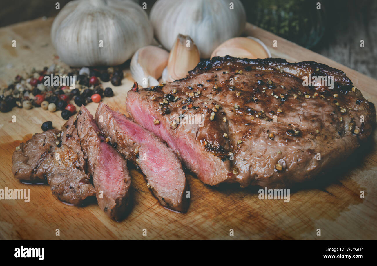 Di medie pepe bistecca fetta tagliata sul piatto di legno con spezie condimento in grigio scuro e di illuminazione del tono. Foto Stock