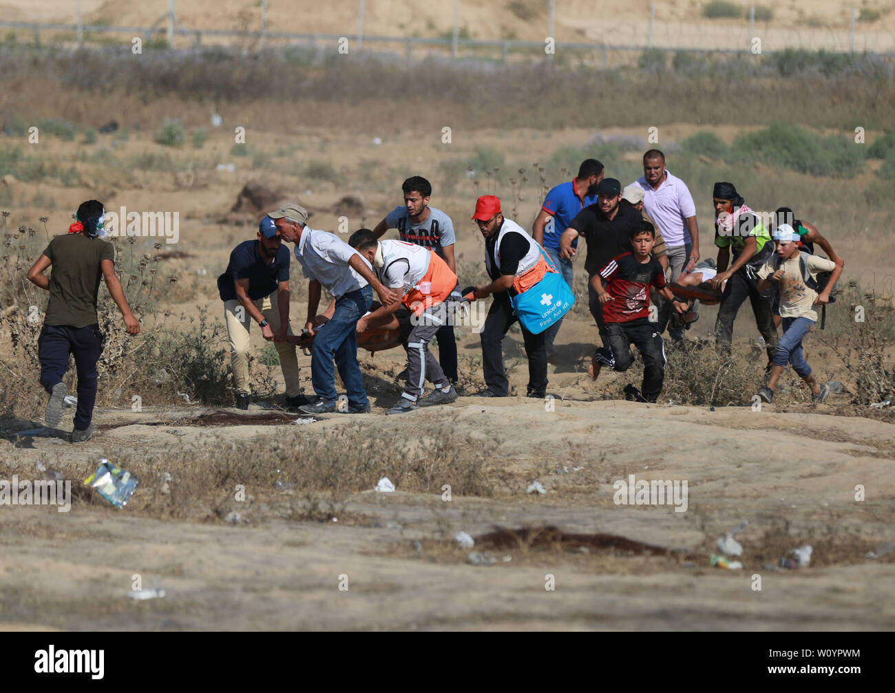 La striscia di Gaza. Il 28 giugno, 2019. I medici palestinesi trasportare feriti durante gli scontri con le truppe israeliane sul confine Gaza-Israel, a est di al-Bureij Refugee Camp nella zona centrale della striscia di Gaza, 28 giugno 2019. Almeno 50 palestinesi sono stati feriti nel venerdì di scontri tra decine di dimostranti e soldati israeliani appostati lungo il confine tra la parte orientale della striscia di Gaza e Israele. Credito: Yasser Qudih/Xinhua/Alamy Live News Foto Stock