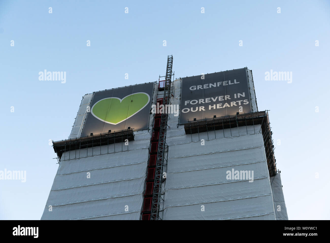 Grenfell Tower, ora coperta, con il simbolico cuore verde visualizzato. "Per sempre nei nostri cuori" Foto Stock