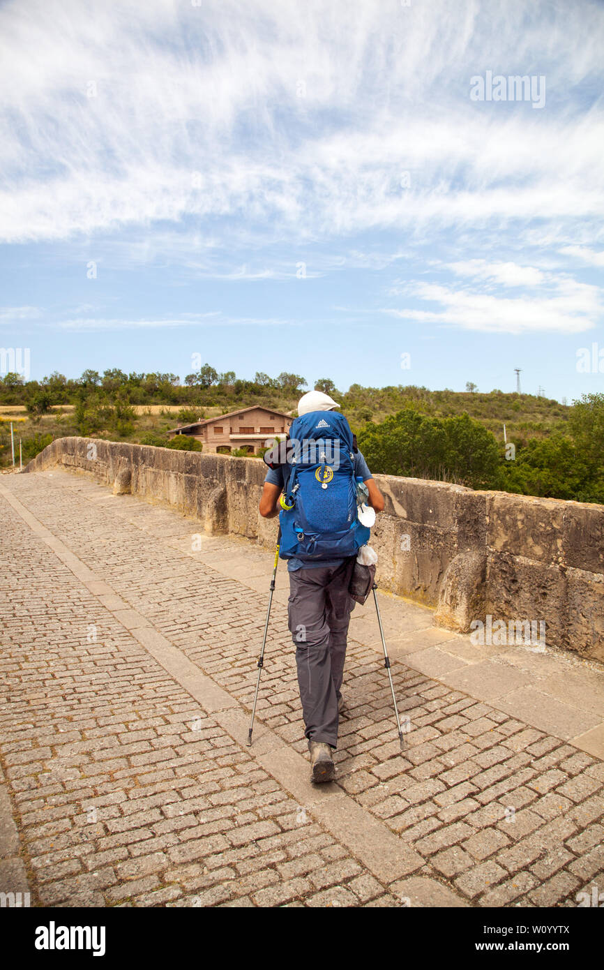 Man Pilgrim camminare sul ponte medievale nella città spagnola di Puente la Reina mentre si cammina il cammino di pellegrinaggio Camino de Santiago in Spagna Foto Stock