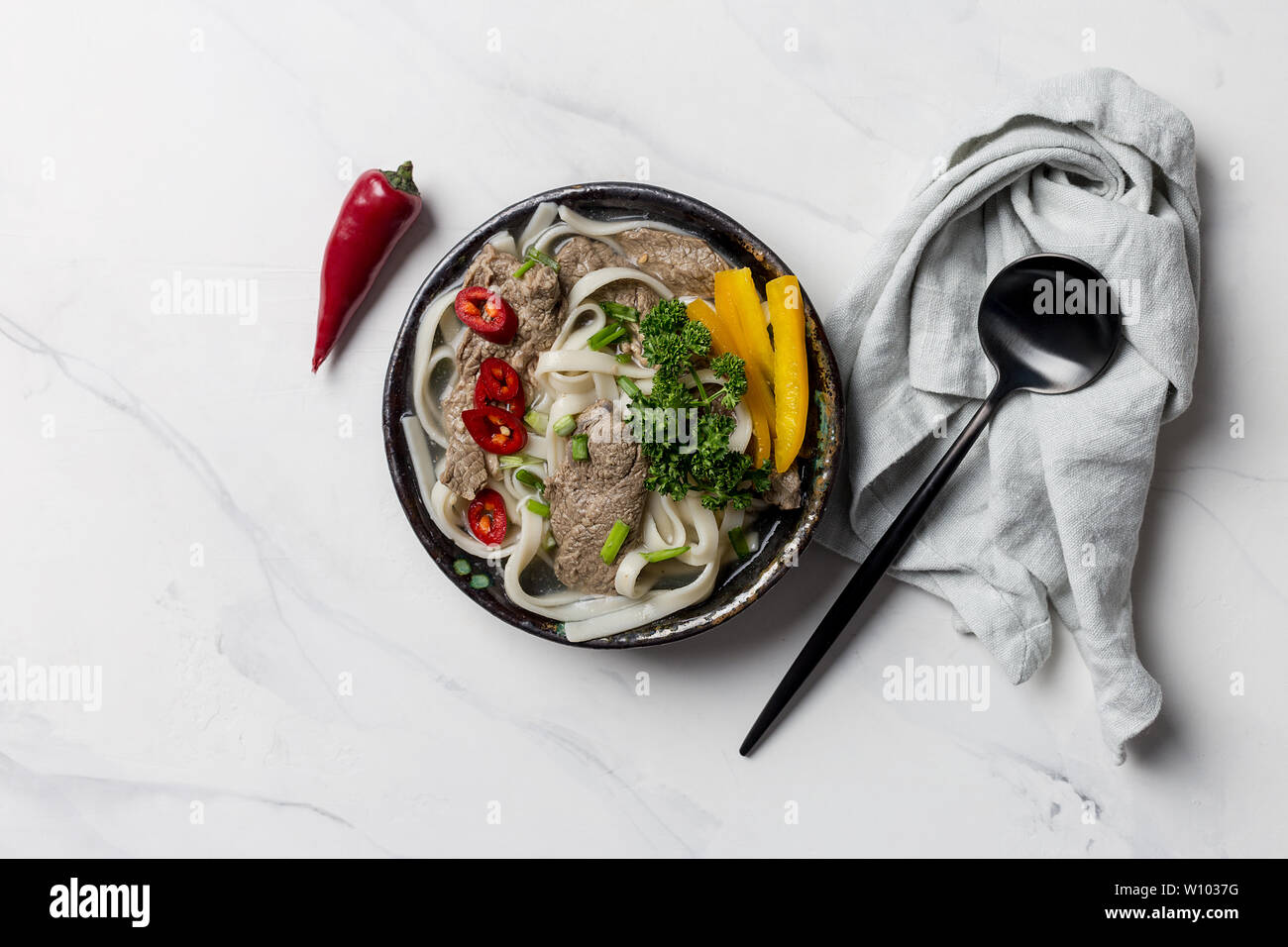 Asian zuppa di noodle, la carne e le verdure nella ciotola con il tovagliolo grigio e posate su sfondo bianco. Parte superiore orizzontale visualizza spazio libero per il testo Foto Stock