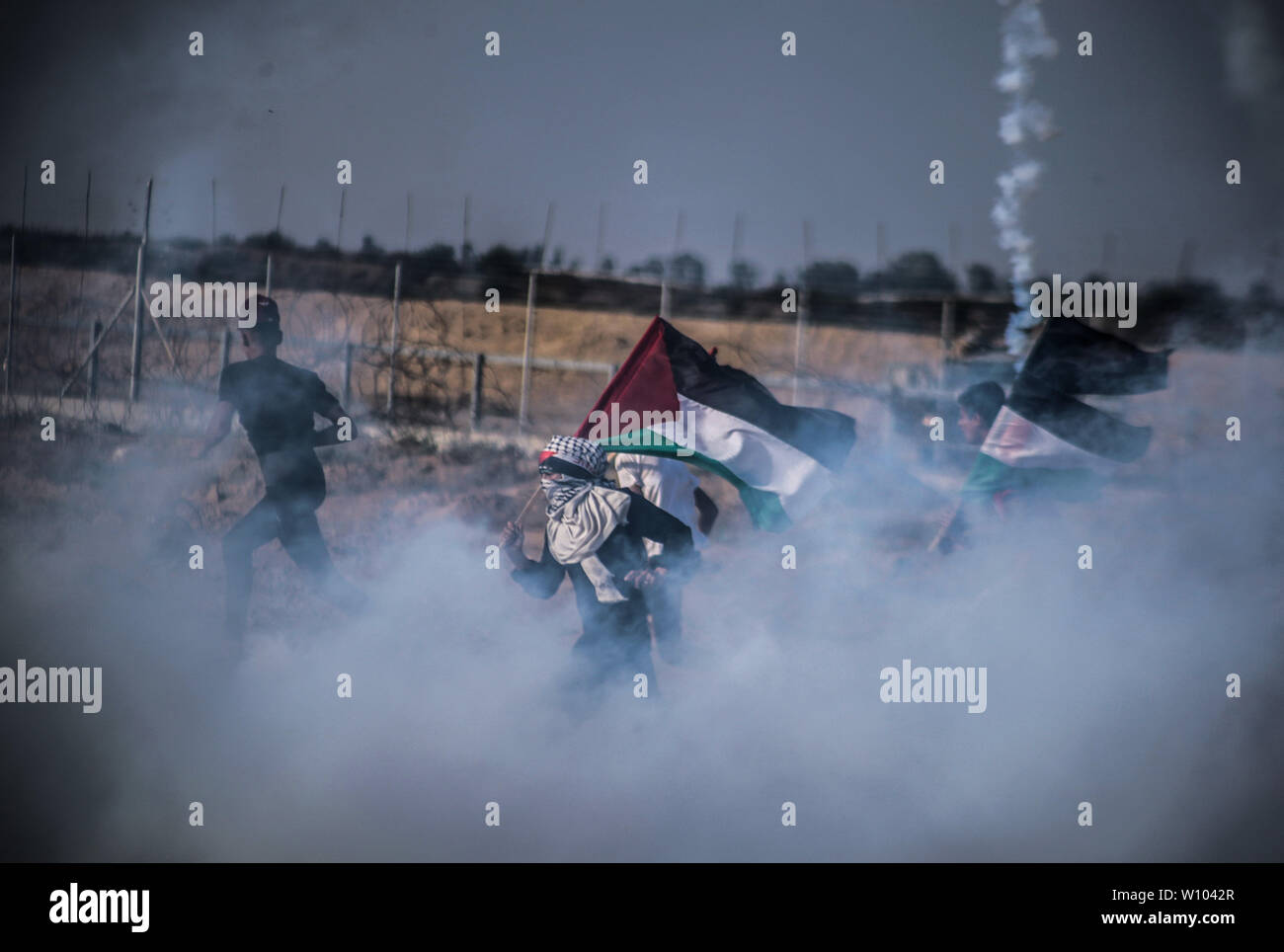 Manifestante palestinese con un flag fugge dal gas lacrimogeni fumo sparato verso di loro durante gli scontri.palestinesi si sono scontrati con le forze israeliane durante una manifestazione di protesta per chiedere la revoca del blocco israeliano su Gaza e impegnativo per il diritto di tornare in patria, al Israel-Gaza recinzione di confine nel sud della striscia di Gaza. Foto Stock