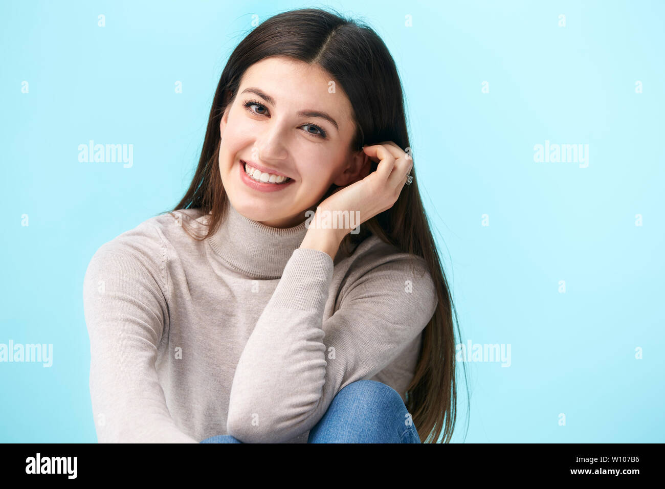 Studio ritratto di una bella donna caucasica, seduto sul pavimento, guardando la telecamera sorridendo, isolato su sfondo blu Foto Stock