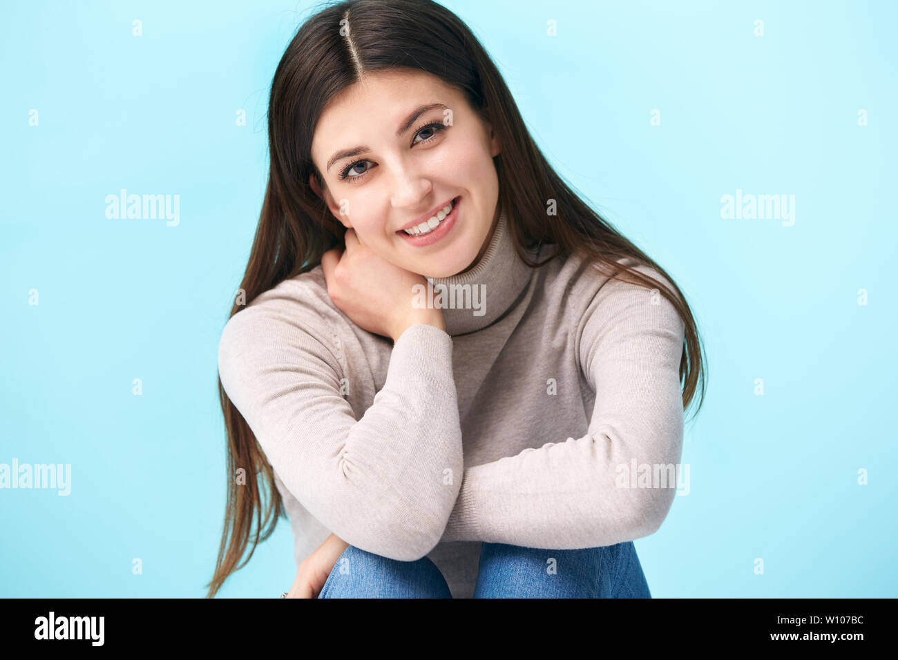 Studio ritratto di una bella donna caucasica, seduto sul pavimento, guardando la telecamera sorridendo, isolato su sfondo blu Foto Stock